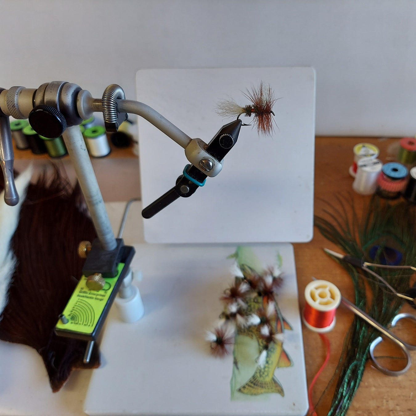 a fly tying vise with a royal coachman fly surrounded by tying tools and materials