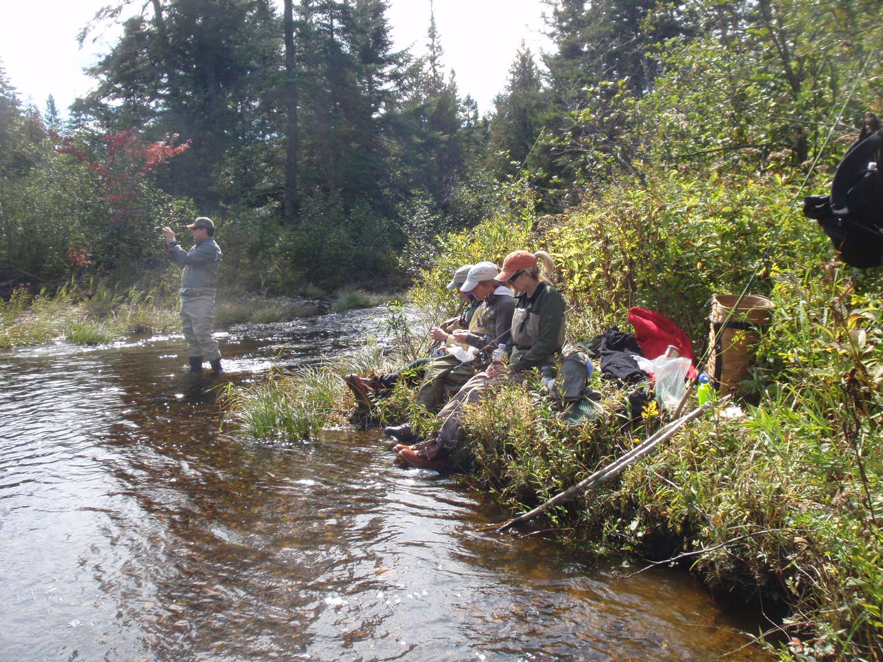 Three people relaxing on the river while one person fishes.