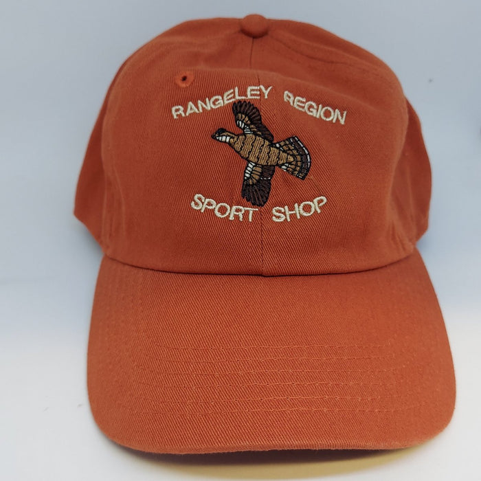 a burnt orange color hat with embroidered flying grouse and the shop name