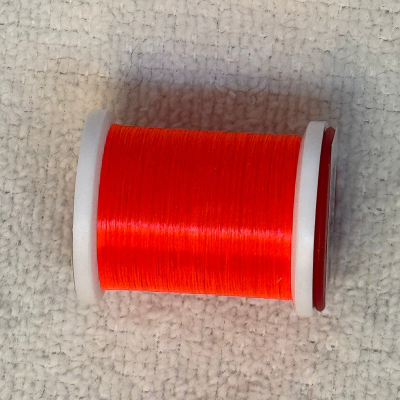70 denier thread spool in red-orange on a light fabric surface