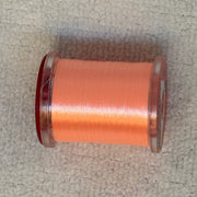 70 denier thread spool in orange on a light fabric surface