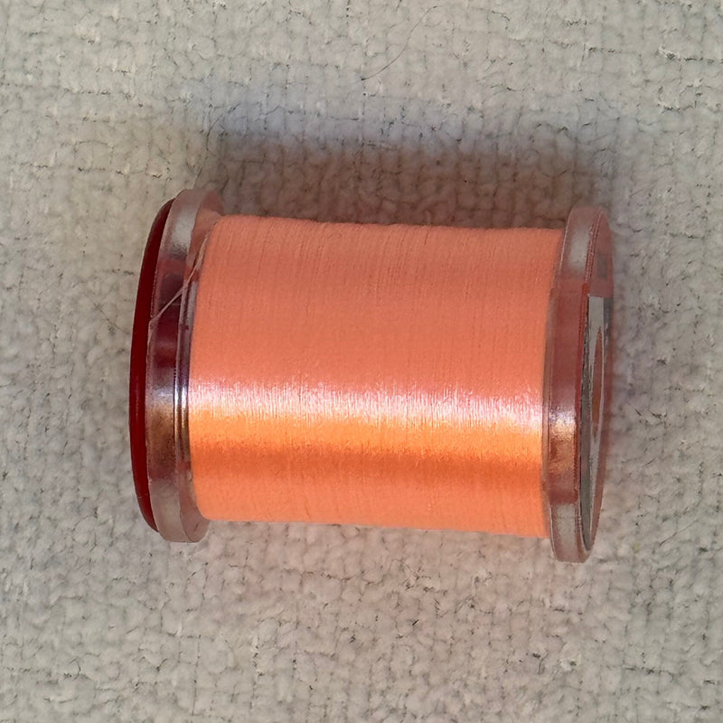 70 denier thread spool in orange on a light fabric surface