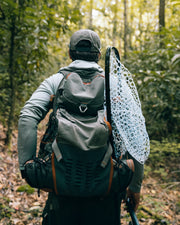 Fishpond Firehole backpack on a person, dark gray with orange accents and mesh pocket