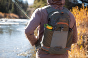 Backpack worn by person outdoors, gray with orange accents and green-lidded top pocket