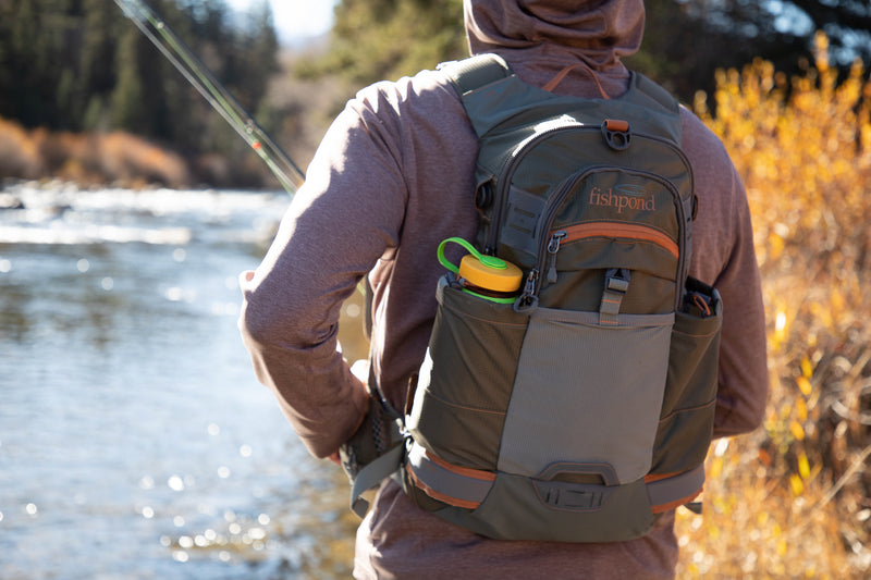 Backpack worn by person outdoors, gray with orange accents and green-lidded top pocket
