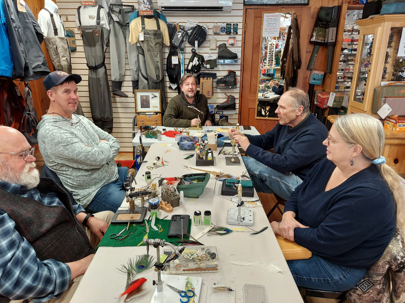 Group of people sitting around a table in a store learning to tie flies