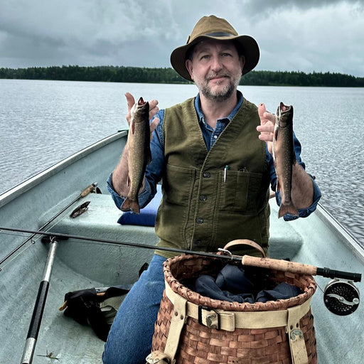 Leslie Hilyard in a boat holding two fish he caught while fly fishing