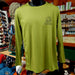 Green long-sleeve shirt on a mannequin in a store setting with various items in the background.
