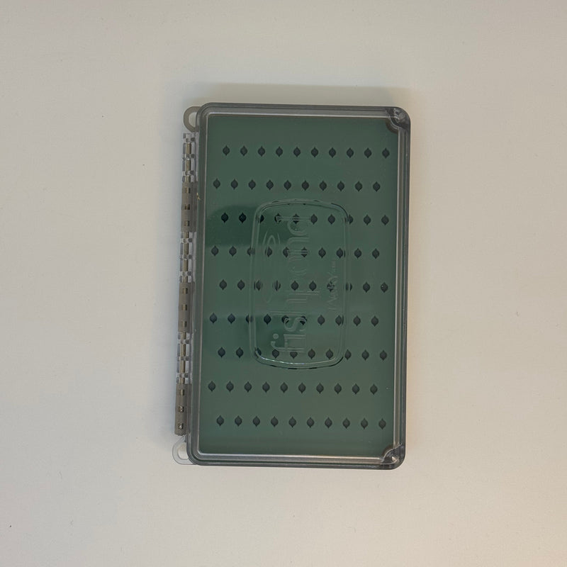 Fly box with closed clear lid and green patterned backing, seen from above