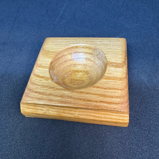 a small wooden square with a round depression used by fly tyers to hold beads, hooks, and other small items