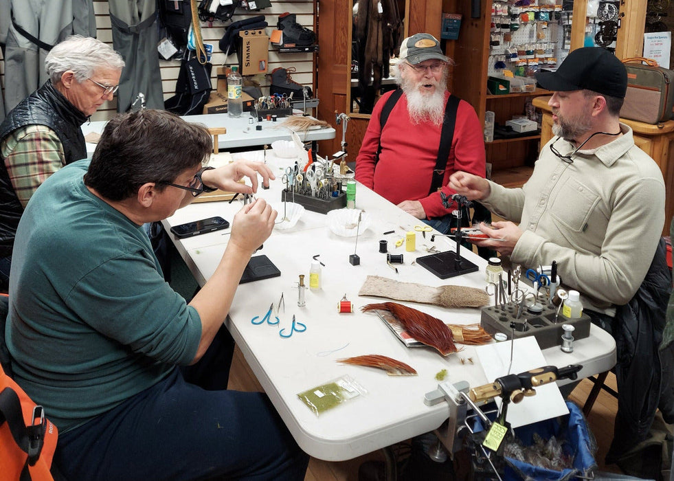 People working on tying flies in a store with various gear displayed.