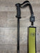 A black REC wading staff with a black retractor and a matching olive green protective sleeve, displayed on a gray wood-look floor. The sleeve features the REC Sports logo.