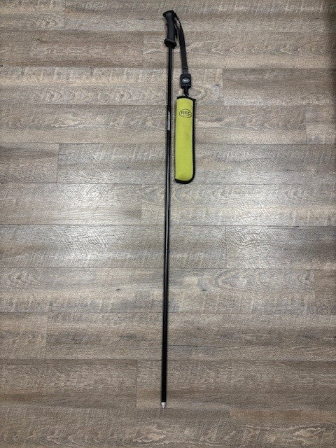 A single wading staff with a bright yellow-green pouch, placed vertically on a gray-brown wood plank floor.