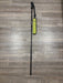 A single wading staff with a bright yellow-green pouch, placed vertically on a gray-brown wood plank floor.