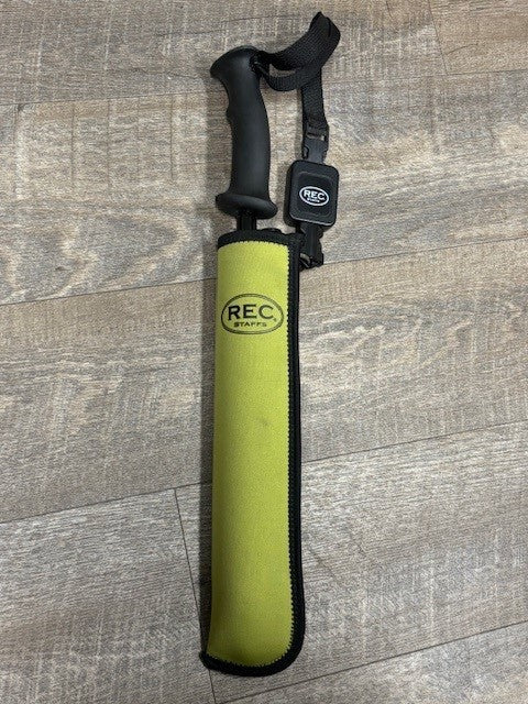 A REC brand wading staff with a black handle and retractor,  with a green protective sleeve on a gray wood-look floor.