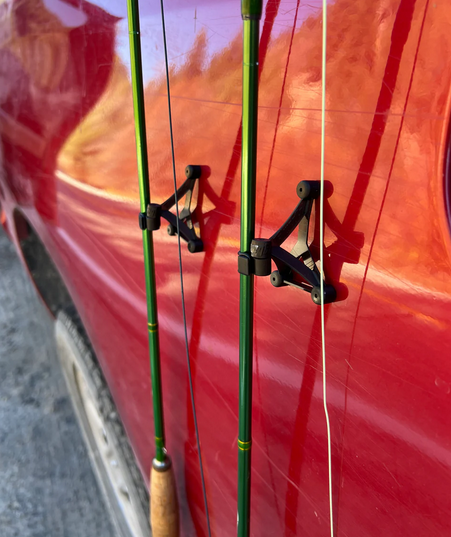 Two green fishing rods attached by the talweg auto roost to a red vehicle.