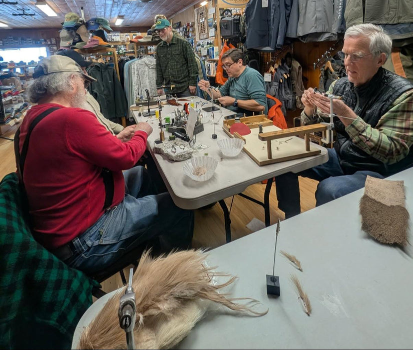 Group of people gathered around a table in a store tying flies.