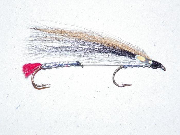 Fishing lure with dark body, red tail, silver hook and feathered streamer.