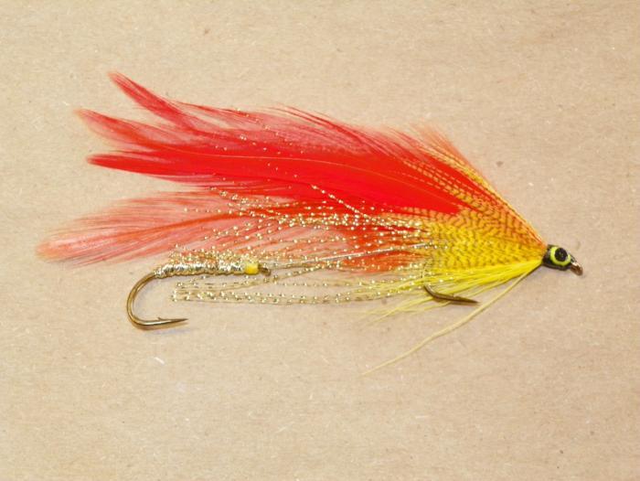Fishing streamer fly with red and yellow feather body, gold sparkle, curved hook