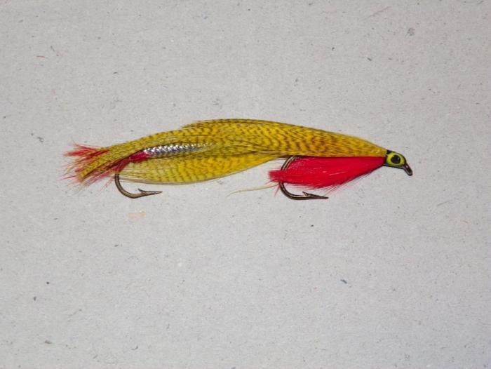 Fishing lure with yellow body, red head, black eye, and feather tail with hooks