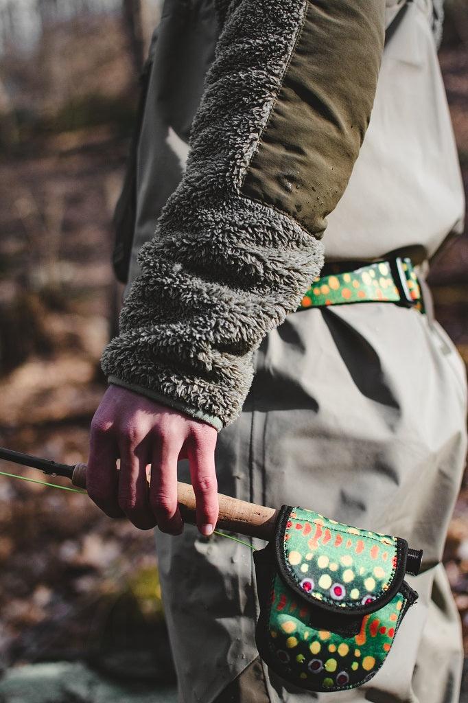 An angler holding a fly rod with the reel protected by a brook trout reel case