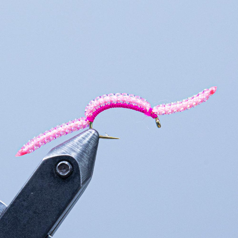 Pink glitter fishing lure worm on hook with curled tail