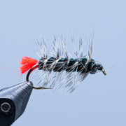 Feather fishing fly lure with dark brown-and-white fuzzy body, red accent tail, black hook