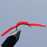 Red glitter fishing lure worm on hook with curled tail